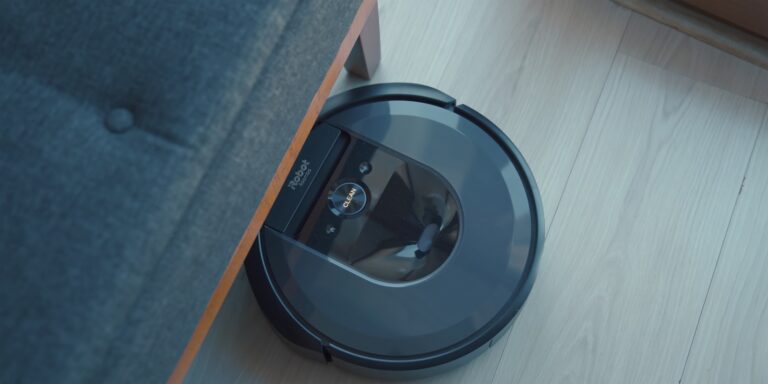 Robot vacuum cleaning a hard floor beside a fabric sofa