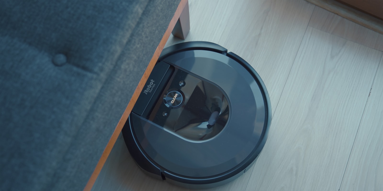 Robot vacuum cleaning a hard floor beside a fabric sofa